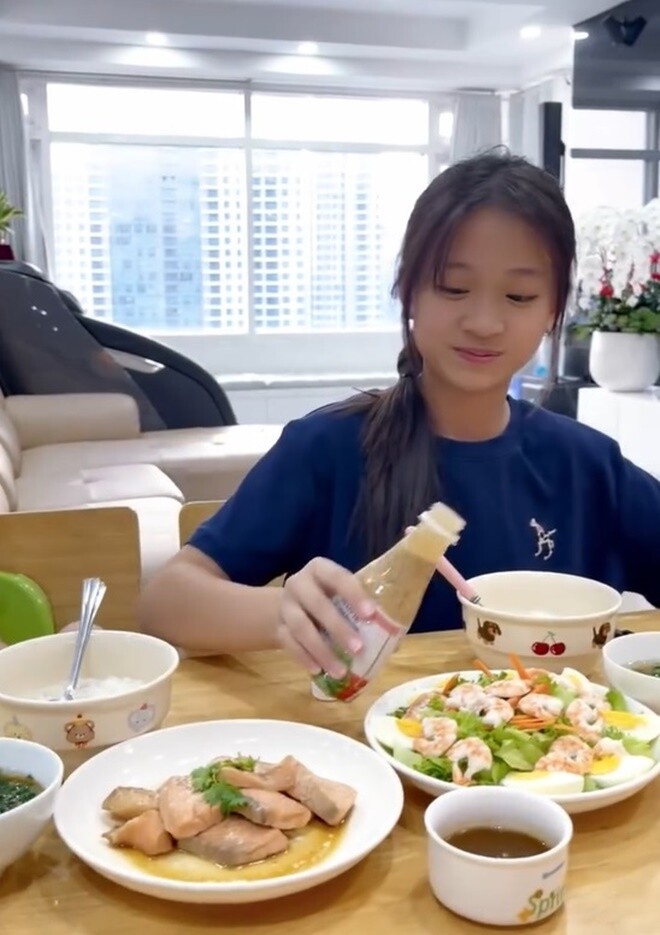 Bé Noel háo hức ngồi vào bàn ăn và cho biết: Hôm nay mình sẽ mukbang đồ ăn của mẹ nấu nha. Cô bé xinh xắn vui vẻ chan nước sốt salad.