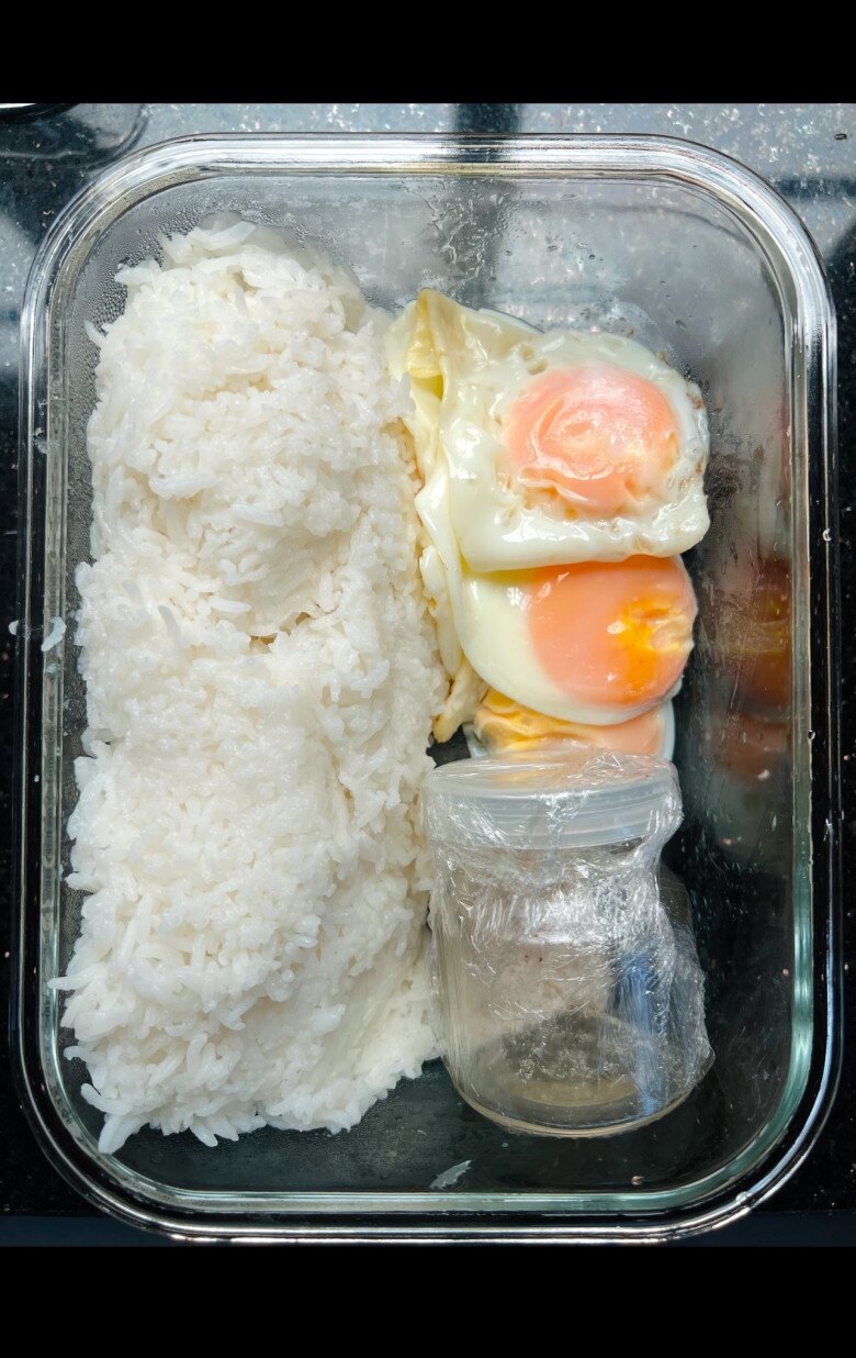 Cơm trắng với trứng ốp la lòng đào hoàn hảo, đi kèm một lọ nước sốt riêng bọc kỹ lưỡng. Vừa tiện mang đi, vừa giữ trọn hương vị khi thưởng thức.