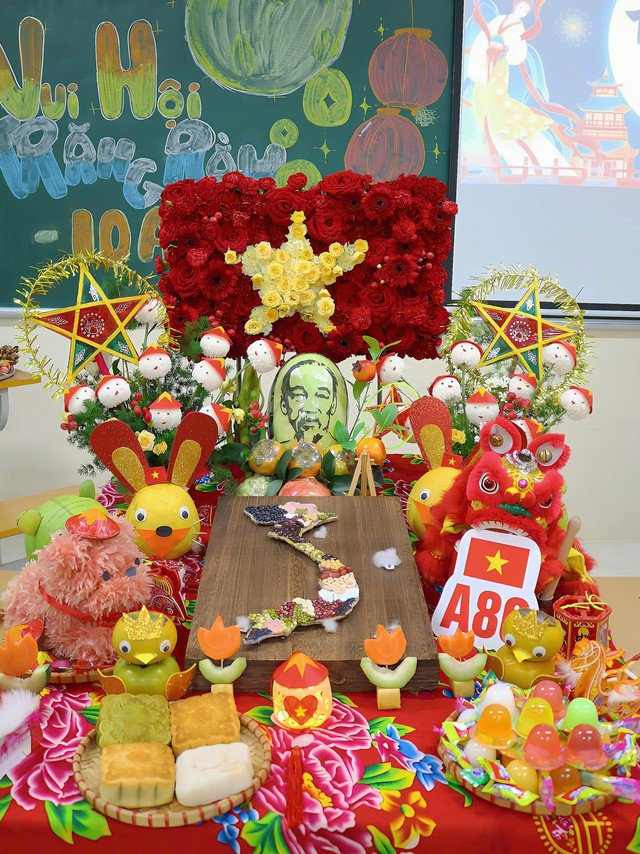 Trên mâm cỗ, cờ đỏ sao vàng kết bằng hoa tươi được đặt ở vị trí trang trọng. Hai bên là hình ảnh các chú bộ đội và đèn ông sao, tượng trưng cho niềm vui, niềm tự hào dân tộc, cũng như lòng biết ơn những người đã hy sinh để bảo vệ Tổ quốc. Ở trung tâm mâm cỗ là quả dưa hấu khắc chân dung Bác Hồ, phía trước nổi bật với chữ A80 – kỷ niệm 80 năm ngày Quốc khánh 2/9. Ảnh NVCC