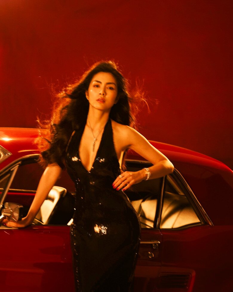 Mái tóc dài uốn gợn sóng nhẹ buông xõa tự nhiên, kết hợp cùng thần thái điềm tĩnh và dáng pose đầy tự tin bên chiếc xe cổ đỏ rực, tạo nên hình ảnh người phụ nữ trưởng thành, gợi cảm mà vẫn sang trọng, quyến rũ.