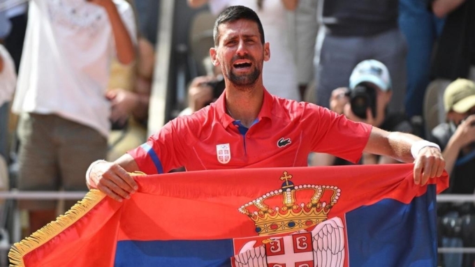 Djokovic mang cờ Serbia khi mừng tấm HC vàng Olympic đầu tiên trong sự nghiệp, tại sân Philippe Chatrier, Paris, Pháp hồi tháng 8 năm ngoái. Ảnh: Reuters