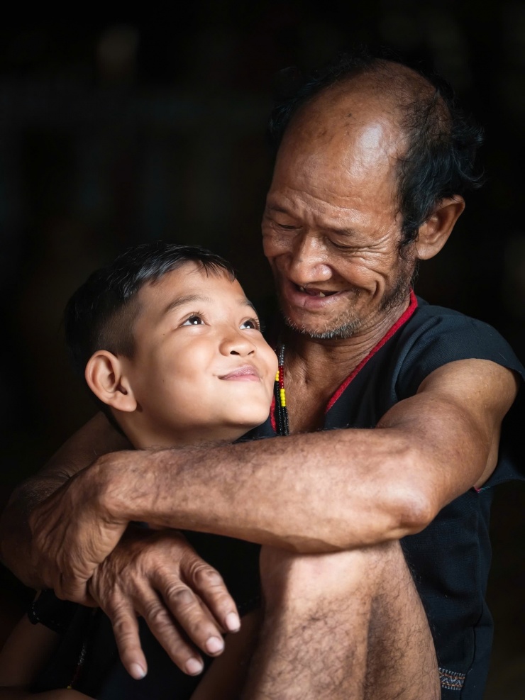 Hơi thở Bahnar trong ánh sáng đại ngàn 6 Trẻ nhỏ trong buôn có sự gắn bó sâu sắc với người lớn. Mối liên kết thiêng liêng ấy càng thêm bền chặt khi chúng được chính những người ông, người cha của mình kiên nhẫn truyền dạy cách làm nghề thủ công truyền thống. Ảnh: Ngô Trần Hải An.