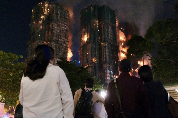 People look on as thick smoke and flames rise during a major fire at the Wang Fuk Court residential estate in Hong Kongs Tai Po district on November 26, 2025. Ảnh: AFP