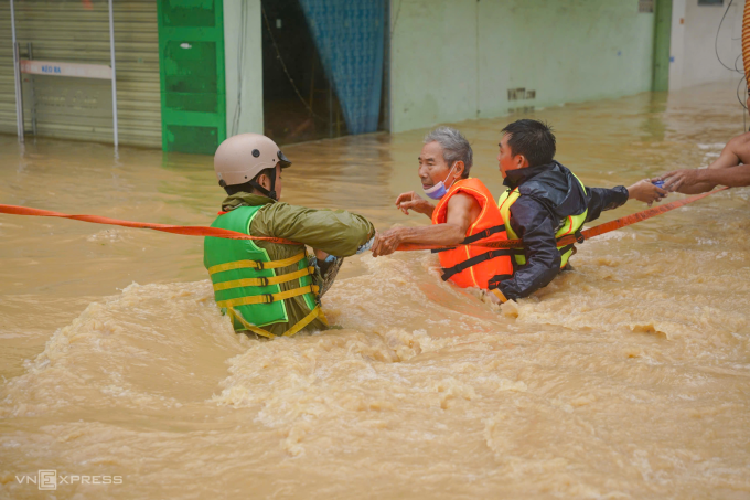 Một người dân được lực lượng chức năng cứu hộ qua dòng nước xiết.