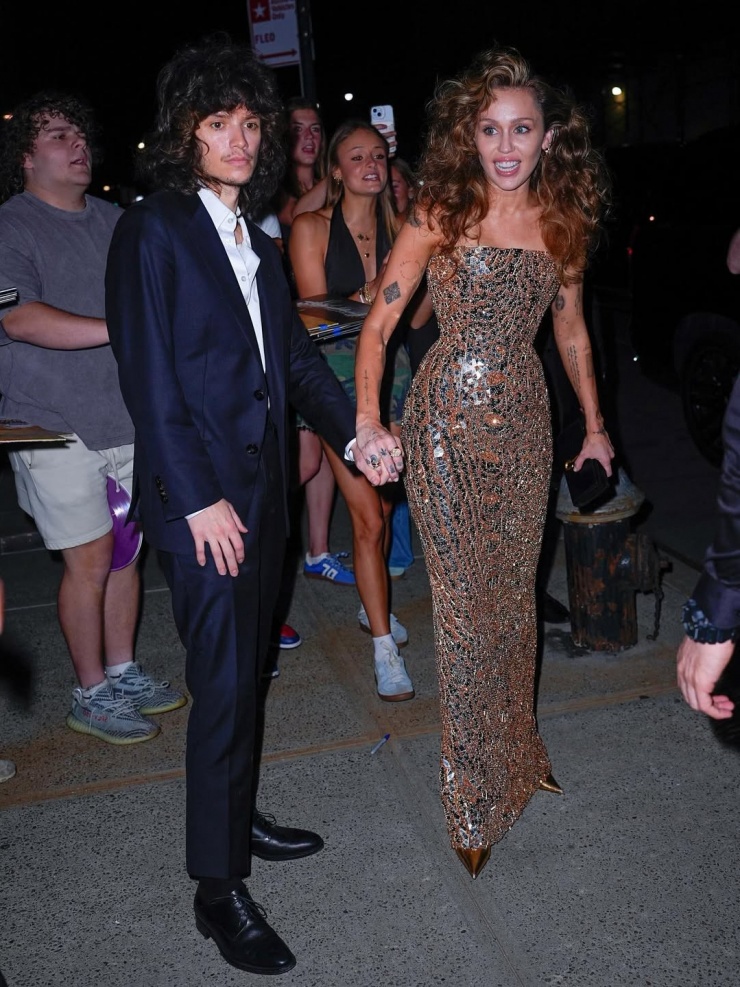 Tháng 6, khi đưa bạn gái đi quảng bá album Something Beautiful, Maxx diện bộ cánh tương tự, thay sneakers bằng giày Tây. Miley ghi điểm bằng bộ đầm quây ngực ánh kim. Cả hai cùng hưởng ứng phong cách cổ điển, để kiểu tóc xoăn bồng bềnh thịnh hàng trong những năm 1980. Ảnh: Celebmafia