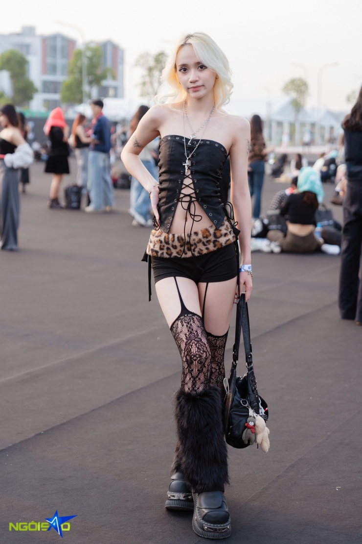 Trần Vy, 24 tuổi, lựa chọn phong cách táo bạo với corset đen buộc dây, phối quần ngắn viền lông họa tiết da báo. Cô kết hợp tất ren đen cùng boots lông bản to, tạo tổng thể nổi loạn, quyến rũ kiểu Y2K.