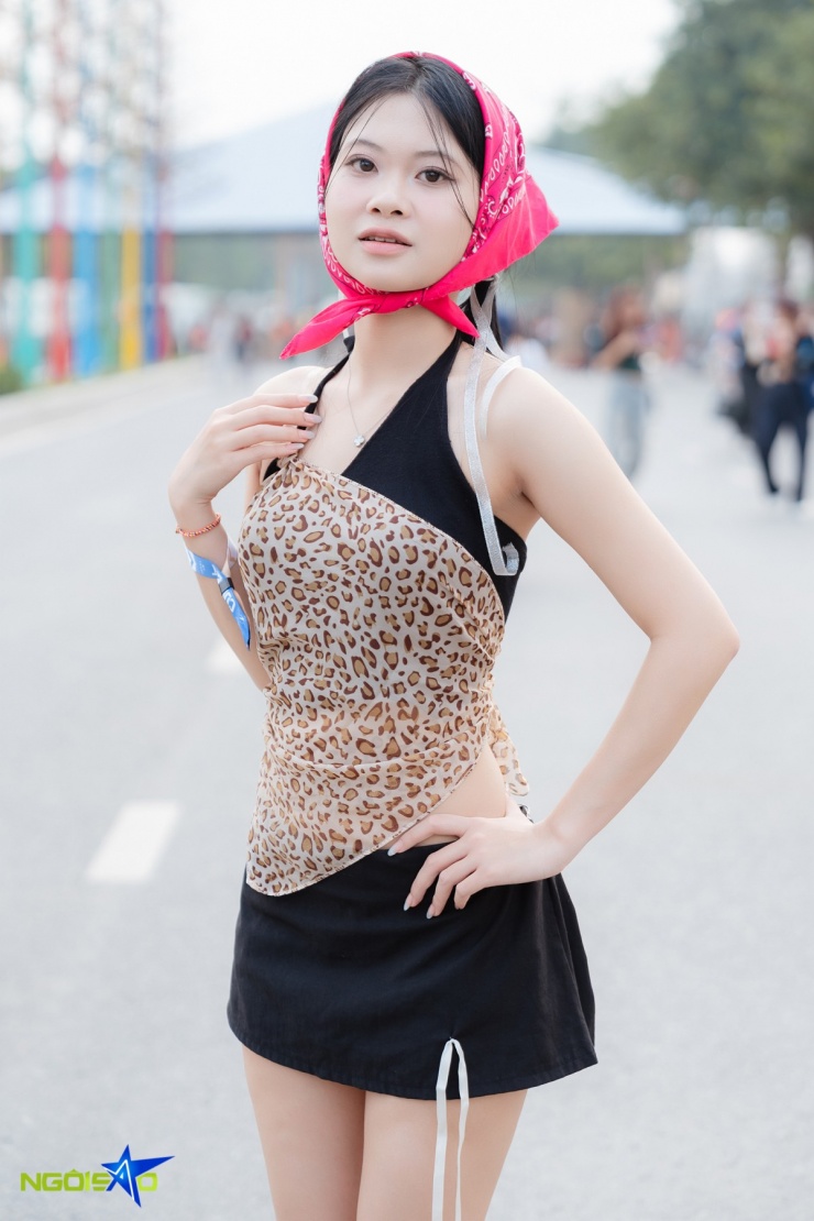 Ngọc Ánh, 21 tuổi, nổi bật với khăn bandana hồng quấn đầu. Cô mặc áo yếm phối họa tiết da báo cách điệu, khoe vai và lưng trần, kết hợp chân váy đen ngắn tối giản.