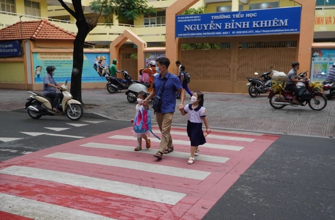 Phụ huynh dắt con qua đường Nguyễn Bỉnh Khiêm, quận 1 cũ, trước trường tiểu học được sơn màu nâu đỏ kết hợp với màu trắng. Ảnh: Giang Anh