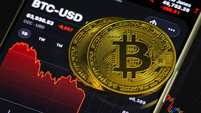 Biểu trưng của Bitcoin được đặt trên màn hình điện thoại theo dõi thị giá tiền số này. Ảnh: CNBC