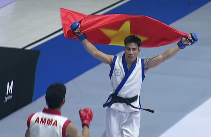 Phạm Văn Nam (phải) cầm cờ Việt Nam chạy quanh sàn thi đấu sau khi thua Norachart Sutharang ở hạng 56kg MMA truyền thống tại SEA Games 33, trong nhà thi đấu MCC Hall ở Nonthaburi, Thái Lan ngày 10/12/2025. Ảnh: Chụp màn hình