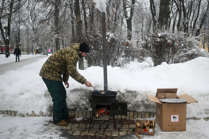 Một tình nguyện viên đang rán bánh trên bếp lò tại một điểm trợ giúp tại công viên ở Kiev ngày 15/1. Ảnh: AFP