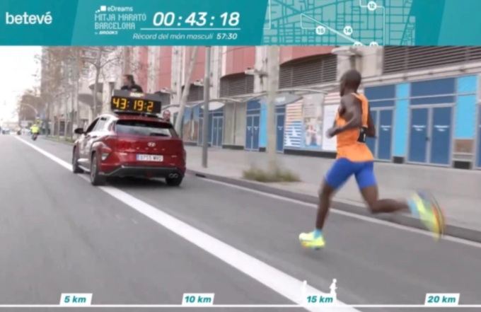 Kiplimo chạy phía sau xe dẫn tốc có đồng hồ cỡ lớn và người ngồi trên nóc ở giải eDreams Mitja Marato tại Barcelona ngày 16/2/2025. Ảnh: eDreams Mitja Marato 2025