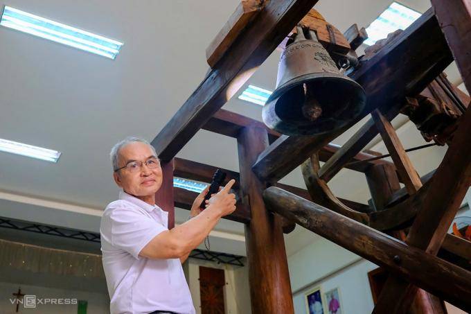 Cha Marcello Đoàn Minh, quản xứ Phú Thượng bên chiếc chuông cổ treo trên giá gỗ tại nhà truyền thống giáo xứ. Ảnh: Nguyễn Đông
