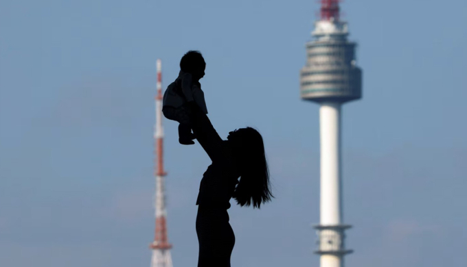 Một người phụ nữ bế cao đứa con nhỏ, in bóng trên nền tháp Namsan tại Seoul, Hàn Quốc, ngày 2/10/2018. Ảnh: Kim Hong-Ji/Reuters