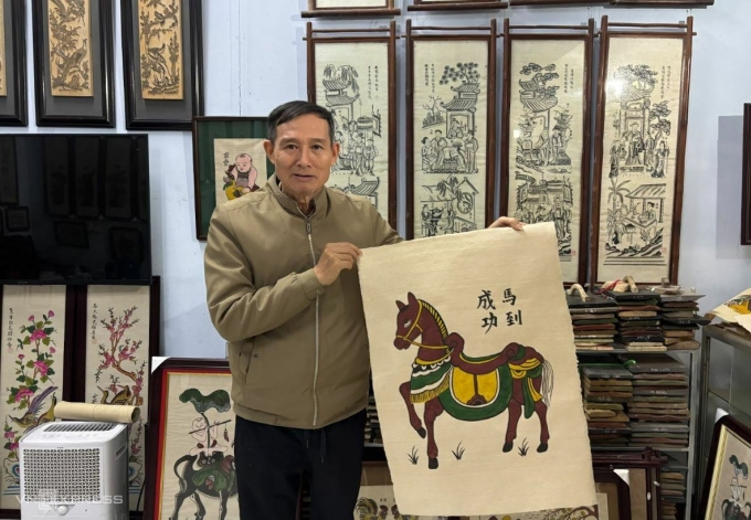 Nghệ nhân Ưu tú Nguyễn Hữu Quả bên bức tranh ‘Mã đáo thành công’- dòng tranh được ưa chuộng mùa Tết Bính Ngọ 2026 . Ảnh: Việt An
