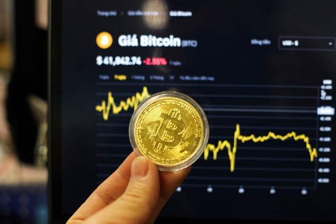 Đồng xu biểu tượng Bitcoin trước biểu đồ diễn biến giá. Ảnh: Khương Nha