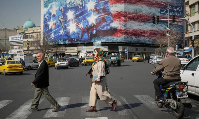 Người dân đi ngang qua một tấm biển tuyên truyền tại thủ đô Tehran, Iran, hôm 22/6 với hình vẽ hình tàu sân bay Mỹ với các máy bay chiến đấu bị hư hỏng trên boong. Ảnh: AP