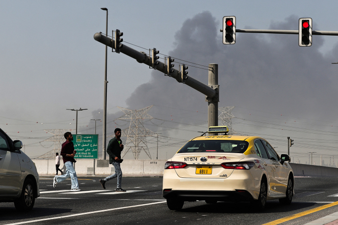People cross a street as smoke rises from the site of a reported Iranian strike in Dubai on March 1, 2026. Ảnh: AFP