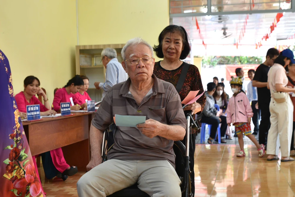 Bà Nguyễn Kim Dung (76 tuổi) đẩy xe lăn đưa chồng là ông Hoàng Đức Chính (86 tuổi, ngụ phường An Khánh) đến tham gia bỏ phiếu. Ảnh: NHẬT DIỄM ba-nguyen-thi-kim-dung-cung-chong.jpg