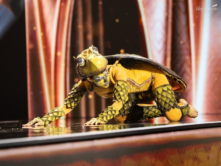 Thí sinh xiếc khỉ, trườn bò trên sân khấu Hoa hậu Hòa bình 12 Đại diện tỉnh Khon Kaen hóa thành chú rùa mai vàng trong phần trình diễn trang phục dân tộc. Theo tín ngưỡng địa phương, rùa là tôi tớ của Chao Pu Fa Rangum, vị thần bảo hộ thiêng liêng của làng. Vì vậy, dân làng giữ gìn truyền thống không làm hại rùa và cùng nhau bảo tồn chúng, biến chúng thành biểu tượng của niềm tin và sự cân bằng giữa con người và thiên nhiên.