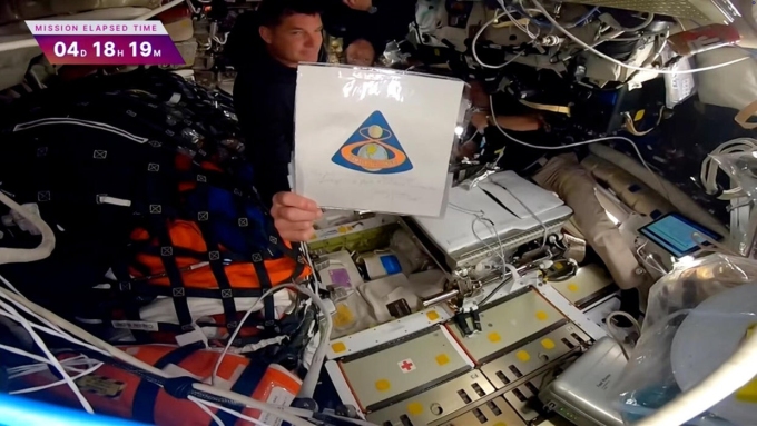 Phi hành gia Reid Wiseman giơ cao huy hiệu của nhiệm vụ Apollo 8, từng bay lên Mặt Trăng năm 1968 và được con trai của Jim Lovell tặng lại cho phi hành đoàn Artemis II. Ảnh: NASA