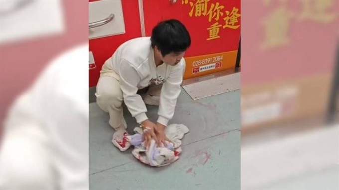 Hồ Tâm Dao lấy áo khoác lau máu trên sàn tàu điện ngầm ở Trùng Khánh hôm 23/3. Ảnh: Sina